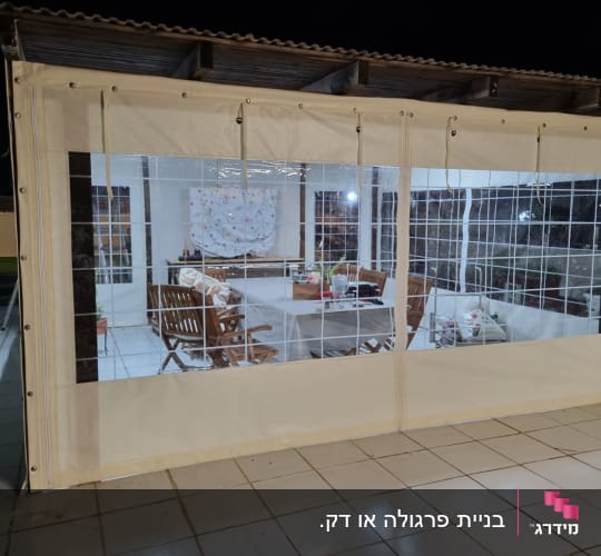 מרפסת מקורה עם ריהוט גן מעץ ומחיצות פלסטיק שקופות